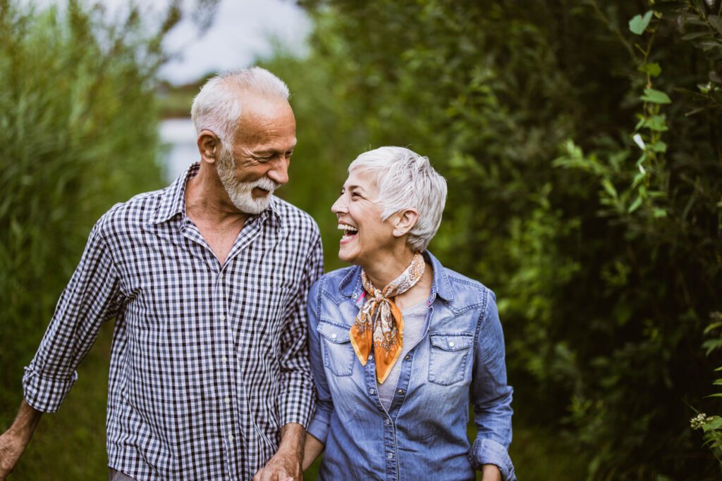 Happy senior couple holding hands while walking and talking in nature.